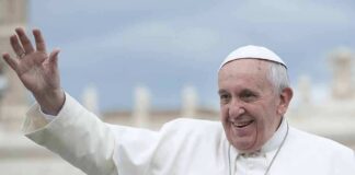 elderly man in white religious attire waving outdoors