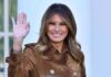 Melania Trump waving and smiling in a brown suede coat