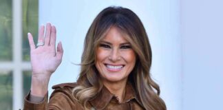 Melania Trump waving and smiling in a brown suede coat