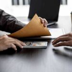 Hands exchanging cash in an envelope at a desk