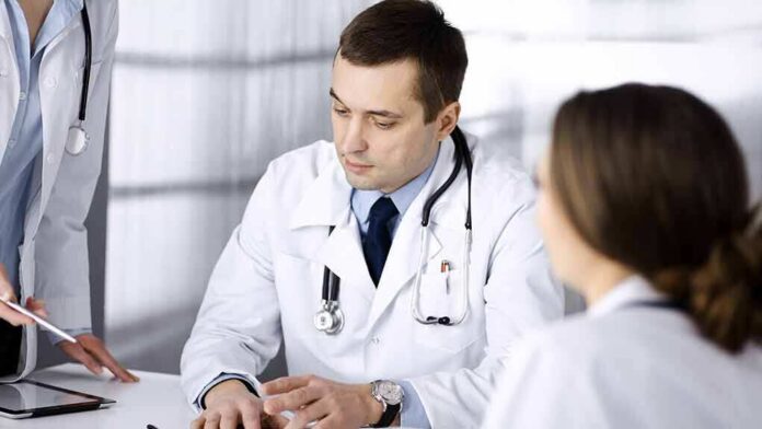 shutterstock_1926064859 Doctors in white coats discuss patient case at a table