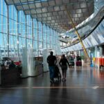 Passengers walk through a modern airport terminal with shops and glass walls