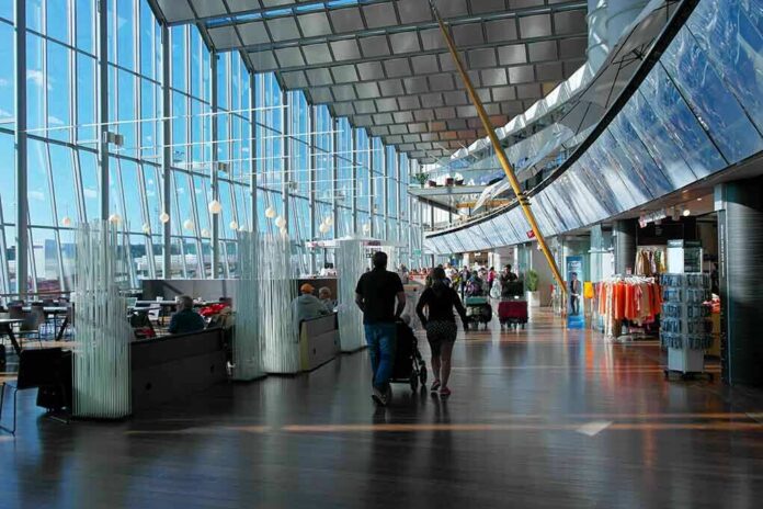 shutterstock_1926188828 Passengers walk through a modern airport terminal with shops and glass walls