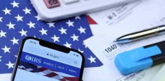 Smartphone showing IRS website on top of tax forms and office supplies