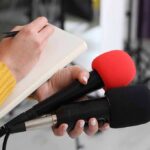 Self-Driving Sting Traps Teens Journalist holding two microphones while writing in a notebook