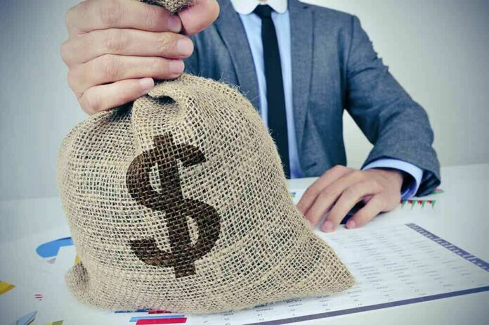 shutterstock_324821675 Businessperson holding a burlap money bag on a desk