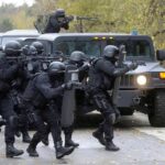 Tactical police team advances from armored vehicle with shields and rifles