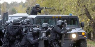 Tactical police team advances from armored vehicle with shields and rifles