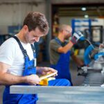 Factory worker in blue overalls measuring metal piece