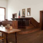 Juror Identities SEALED After Mob Uproar Interior of a historic courtroom with wooden furniture and an American flag