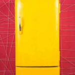 Yellow retro refrigerator against a pink geometric wall