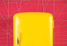 Freezer Corpse Exposes Social Security Hole Yellow retro refrigerator against a pink geometric wall