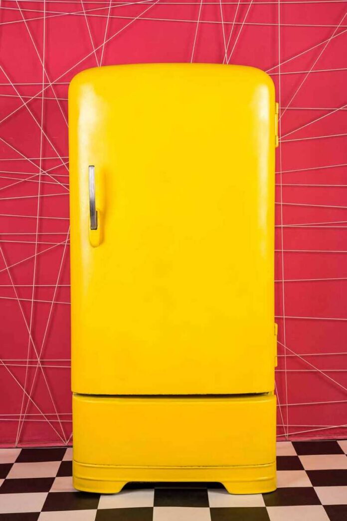 shutterstock_746615260 Yellow retro refrigerator against a pink geometric wall