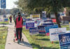 Person walking with stroller past numerous election campaign signs.