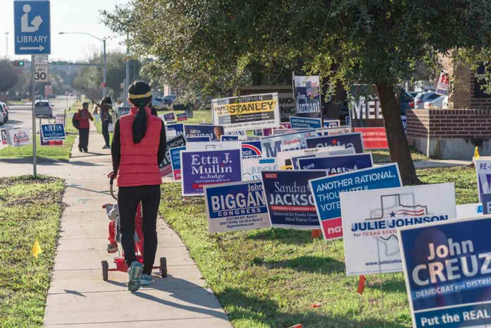 1039327252 Person walking with stroller past numerous election campaign signs.