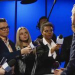 Journalists interview a man in a suit with microphones