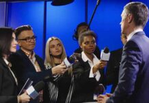 Journalists interview a man in a suit with microphones