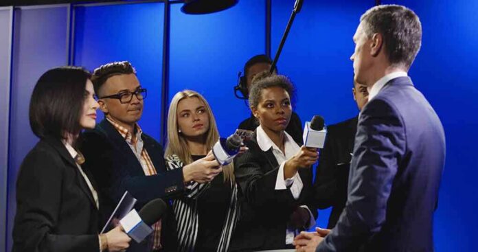 Journalists interview a man in a suit with microphones