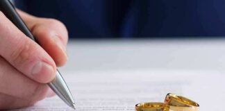 Hand signing a document beside two gold wedding rings
