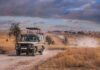 Safari vehicle on a dusty track in a dry savanna landscape