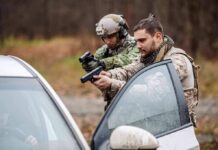 ICE Nabs Canadian Activist At The Border Two armed men in tactical gear aiming pistols at a car