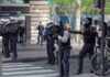 Riot police in helmets line a city street during an operation