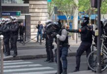 Riot police in helmets line a city street during an operation