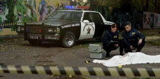 Crime scene with police car and two investigators by a covered body
