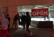 Milan Meltdown Triggers Army Patrols People outside a storefront with broken glass at night