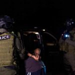 Police officers detain a handcuffed person at night