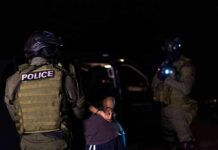 Police officers detain a handcuffed person at night