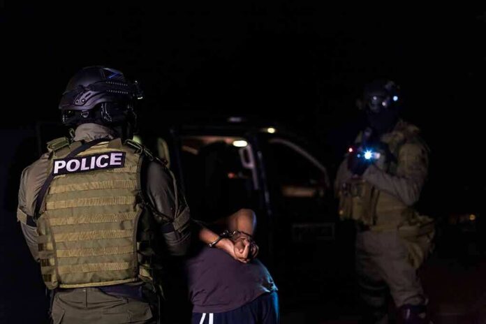 Police officers detain a handcuffed person at night