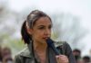 AOC’s Next Move: White House Or Schumer? AOC speaking into a handheld microphone outdoors