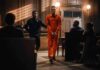 Defendant in orange jumpsuit escorted by officer in courtroom
